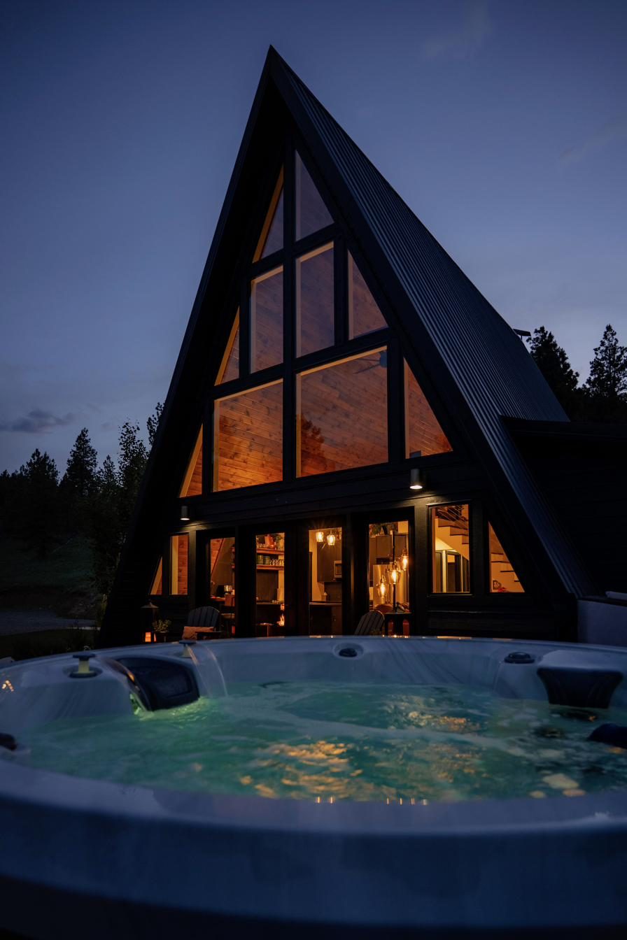 A-frame glowing at dusk with lit hot tub